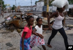 FILE - Girls holding hands are led past a burnt car blocking the street as they evacuate the Delmas 22 neighborhood to escape gang violence in Port-au-Prince, Haiti, May 2, 2024.