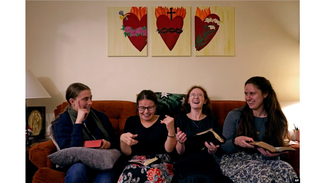 Mahasiswa Benedictine College, dari kiri: Ashley Lestone, Hannah Moore, Niki Wood, dan Madeline Hays tertawa bersama saat mereka membaca kitab doa mereka sebelum berdoa sore di sebuah kapel di rumah mereka di Atchison, Kansas, 3 Desember 2023.(AP/Charlie Riedel)