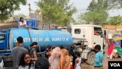 Mushrat Praveen, a resident of a working class neighborhood in Delhi, clambers on top of a tanker that comes to supply water as people scramble to fill buckets. (Anjana Pasricha/VOA)