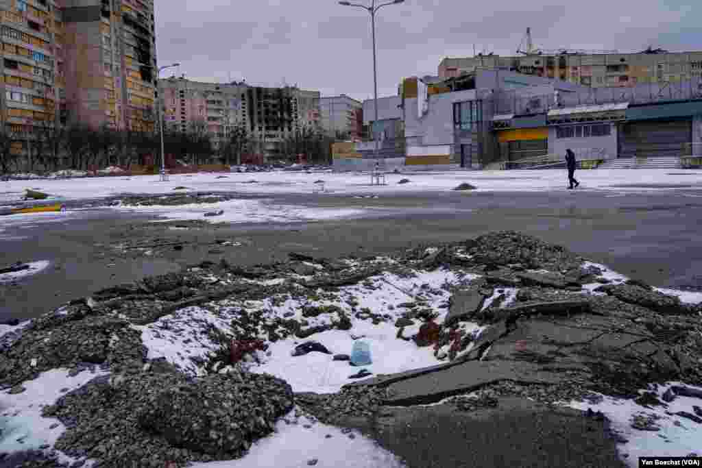 A man passes by a crater created when a missile hit a parking lot in Saltivka, a residential district of Kharkiv, Feb. 15, 2023. 