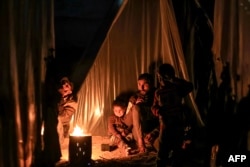 A man sits with children by a fire outside one of the tents housing Palestinians displaced by the conflict in Gaza between Israel and the Palestinian Hamas movement, in Rafah in the southern Gaza Strip on Dec. 18, 2023.