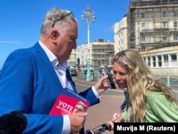 Anna Comaschi engages with Steve Endacott, an independent candidate in the Brighton Pavilion race, and his AI avatar, in Brighton, Britain, June 17, 2024. (REUTERS/Muvija M)
