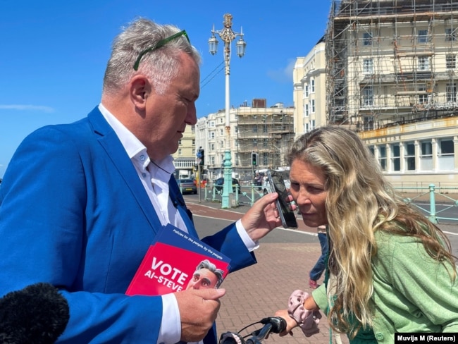 Anna Comaschi engages with Steve Endacott, an independent candidate in the Brighton Pavilion race, and his AI avatar, in Brighton, Britain, June 17, 2024. (REUTERS/Muvija M)