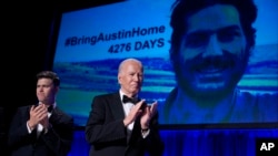 Host Colin Jost, left, and President Joe Biden applaud as an image of Austin Tice, an American journalist detained in Syria, appears on screen at the White House Correspondents' Association Dinner, April 27, 2024, in Washington. 