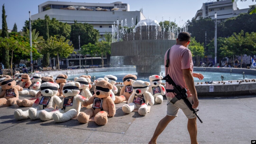 An off-duty Israeli soldier walks by blindfolded teddy bears with photos of Israelis held captive in Gaza, in Tel Aviv, Israel, Oct. 25, 2023. The government's lack of help for those in need have left survivors to mourn on their own and volunteers to take on recovery efforts.