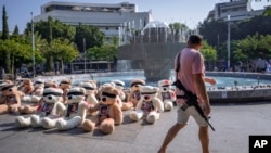 An off-duty Israeli soldier walks by blindfolded teddy bears with photos of Israelis held captive in Gaza, in Tel Aviv, Israel, Oct. 25, 2023. The government's lack of help for those in need have left survivors to mourn on their own and volunteers to take on recovery efforts.