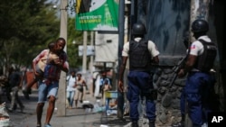 FILE - A parent, holding his child, runs past police carrying out an operation against gangs in the Bel-Air area of Port-au-Prince, Haiti, March 3, 2023. Prime Minister Ariel Henry signaled March 17, 2023 that he wants to mobilize Haiti’s military to help fight the gangs. 