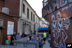 Pelanggan duduk di teras belakang Palmer's Bar, yang bersebelahan dengan masjid Dar Al-Hijrah di Minneapolis, Kamis, 12 Mei 2022. Adzan terdengar tiga kali sehari dari teras bar ini. (AP/Jessie Wardarski)