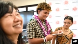 Lahainaluna High School 2024 graduate Talan Toshikiyo, center, stands by sister Taleah Toshikiyo and school college and career counselor Ginny Yasutake as he opens his scholarship announcement in the school's library July 31, 2024, in Lahaina, Hawaii. 