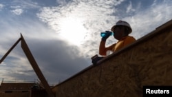 FILE - A construction worker drinks a cold beverage during a heat wave where temperatures rose to over 110 degrees Fahrenheit in Scottsdale, Ariz., July 28, 2023. A new study says climate change will cut incomes and also impact worker productivity.