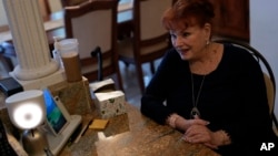 Deanna Dezern, 83, prompts her ElliQ, left, a tabletop device that uses artificial intelligence to conduct human-like conversations, to speak to visiting journalists, inside her home in Tamarac, Florida, Dec. 7, 2023. 