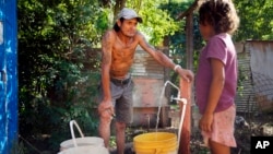 Carmelo Del Valle and his daughter, who were displaced from their home by the rising waters of the Paraguay River, fill buckets with water in Asuncion, Paraguay, March 18, 2023. (AP Photo/Jorge Saenz)