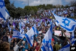 Israelis wave national flags during protest against plans by Prime Minister Benjamin Netanyahu's new government to overhaul the judicial system, outside the Knesset, Israel's parliament, in Jerusalem, Monday, Feb. 13, 2023. (AP Photo/Ohad Zwigenberg)