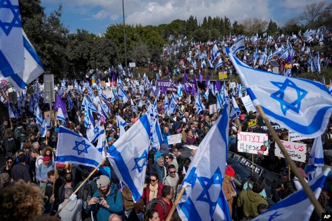 Israelis wave national flags during protest against plans by Prime Minister Benjamin Netanyahu's new government to overhaul the judicial system, outside the Knesset, Israel's parliament, in Jerusalem, Monday, Feb. 13, 2023. (AP Photo/Ohad Zwigenberg)