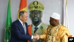 In this photo released by Russian Foreign Ministry Press Service, Russian Foreign Minister Sergey Lavrov, left, and Guinea's foreign minister Morissanda Kouyate shake hands near a portrait of Guinea's President Mamadi Doumbouya in Conakry, Guinea, on June 3, 2024.