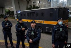 Police officers stand guard as an armored prison van carrying activist publisher Jimmy Lai leaves West Kowloon Magistrates' Courts, in Hong Kong, Dec. 18, 2023.