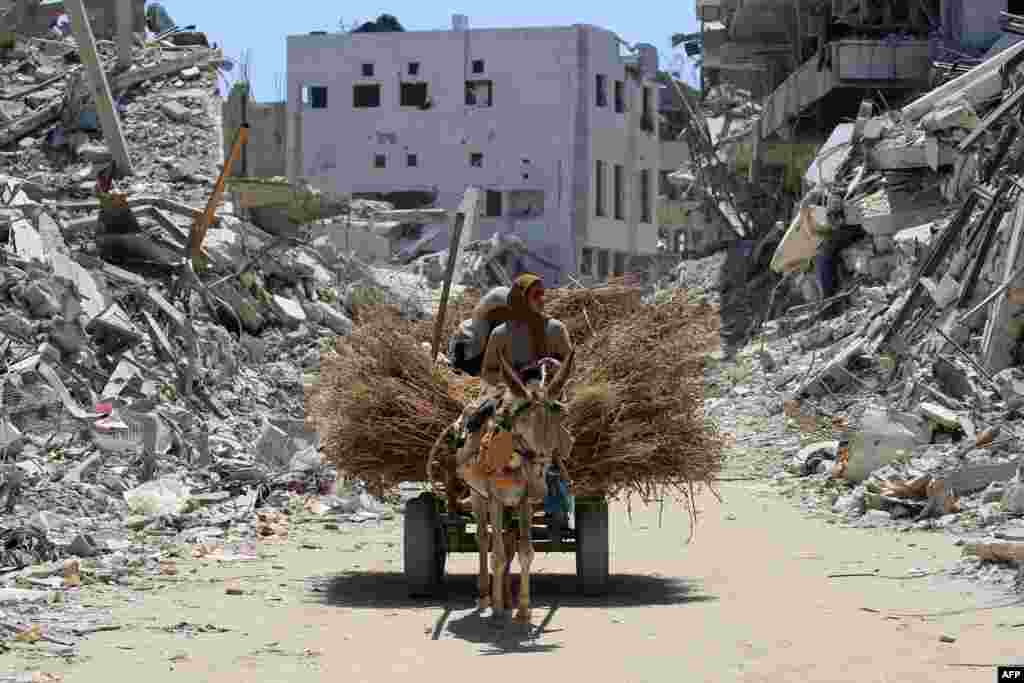 Women transport hay on a donkey-pulled cart along a devastated street in Khan Yunis in the southern Gaza Strip.