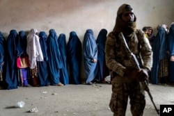 Seorang anggota pasukan Taliban berjaga-jaga saat para para perempuan menunggu menerima jatah makanan yang didistribusikan oleh kelompok bantuan kemanusiaan, di Kabul, Afghanistan, 23 Mei 2023. (Foto: AP)