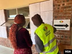 A Zimbabwe Electoral Commission official assists a voter in finding her name on a voter roll at a polling station in Harare, Aug. 24, 2023. (Columbus Mavhunga/VOA)