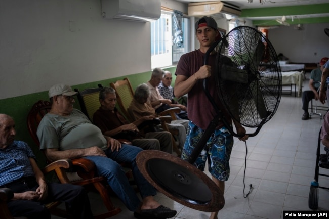 FILE - Aid worker Roger Duvan Lagunes carries a fan into an elderly shelter in Veracruz, Mexico, on June 16, 2024. (AP Photo/Felix Marquez)