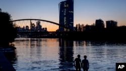 Two boys stand at the river Main near the European Central Bank in Frankfurt, Germany, after sunset, Sept. 8, 2023.