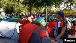 Seorang perempuan yang membawa bendera Prancis berjalan melewati kumpulan tenda yang dipasang oleh LSM di alun-alun Place de la Bastille, Paris, sebagai bagian dari kampanye menyoroti isu tunawisma di Paris pada 6 Agustus 2024. (Foto: Reuters/Abdul Saboor)