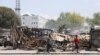 FILE - People walk past remains of vehicles near the presidential palace, after they were set on fire by gangs, as violence spreads and armed gangs expand their control over the capital, in Port-au-Prince, Haiti, March 25, 2024.