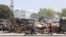 FILE - People walk past remains of vehicles near the presidential palace, after they were set on fire by gangs, as violence spreads and armed gangs expand their control over the capital, in Port-au-Prince, Haiti, March 25, 2024.