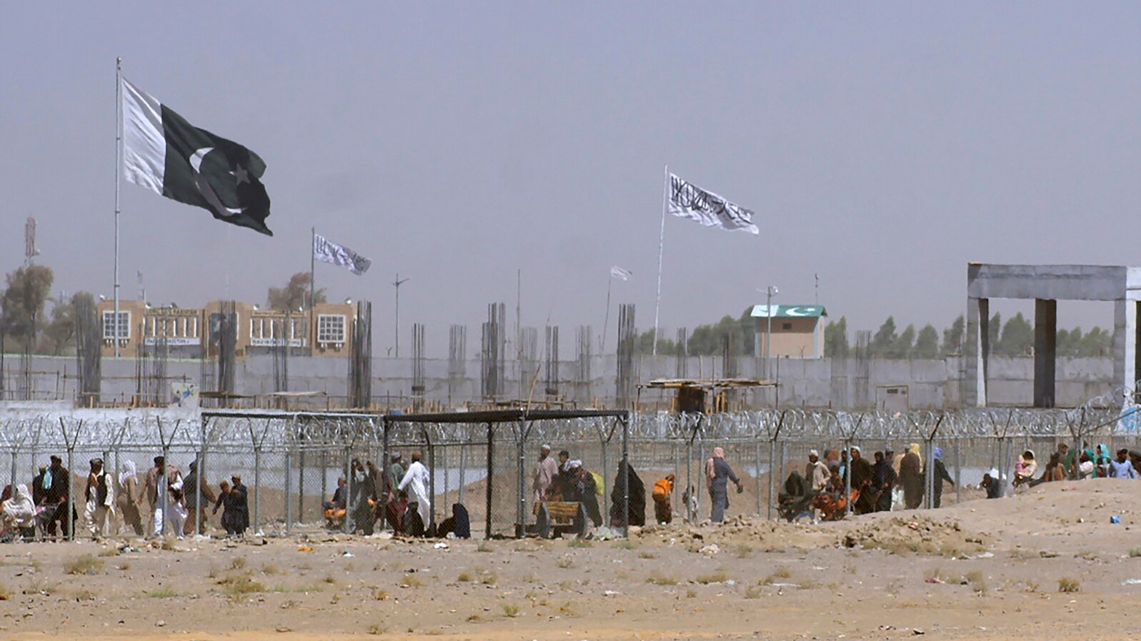 FILE - Pakistani and Taliban flags flutter on their respective sides while people walk through a security barrier to cross the Pakistan-Afghan border in Chaman, Pakistan, Aug. 18, 2021.