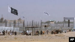 FILE - Pakistani and Taliban flags flutter on their respective sides while people walk through a security barrier to cross the Pakistan-Afghan border in Chaman, Pakistan, Aug. 18, 2021.