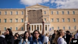 Seorang demonstran mengangkat plakat bertuliskan "Yunani memakan anak-anak mereka" saat protes untuk korban bencana kereta di depan Parlemen, Athena, 8 Maret 2023. (Foto: AP)