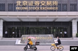 Sejumlah orang mengendarai motor melintas di depan Bursa Saham Beijing di Beijing, China, 9 Juli 2024. (Foto: Adek Berry/AFP)