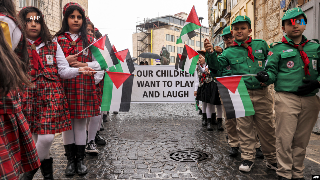 Desde Palestina: Jóvenes palestinos miembros del movimiento scout sostienen pancartas condenando y pidiendo el fin del conflicto en la Franja de Gaza, en la ciudad bíblica de Belén, en la Cisjordania ocupada el 24 de diciembre de 2023.