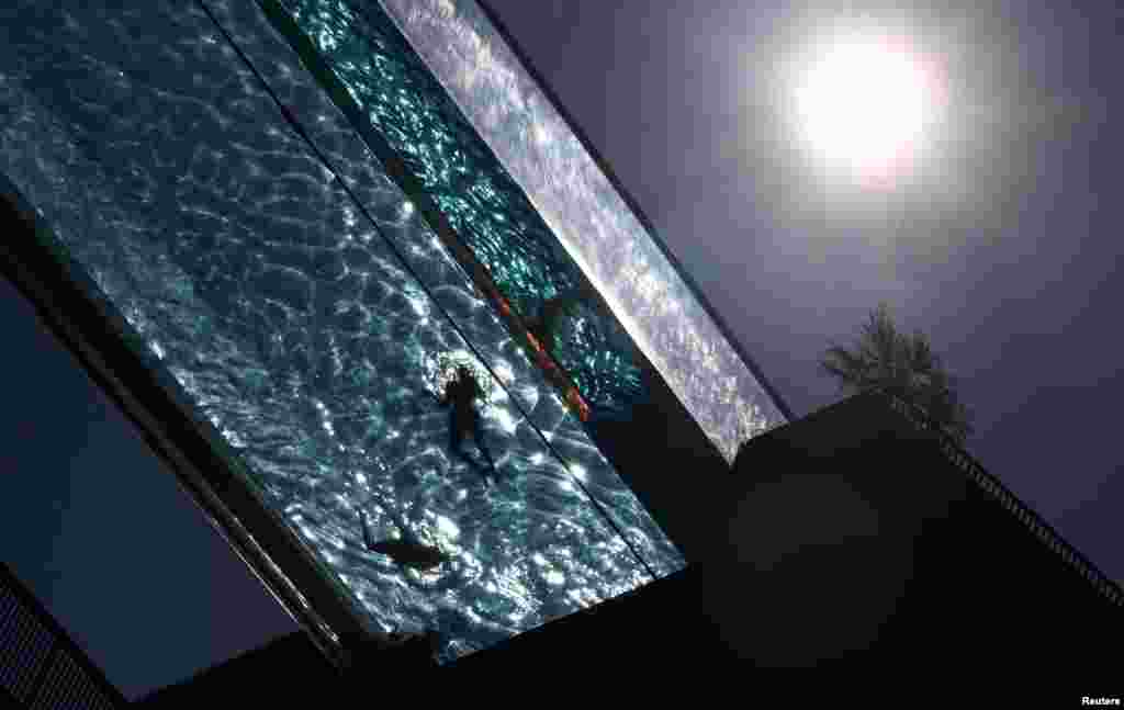 People relax in a swimming pool suspended between high-rise residential buildings at Embassy Gardens as the hot weather continues in London.