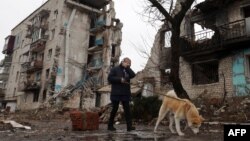 A woman walks her dog past her residential building destroyed as a result of shelling earlier in the war in the town of Izyum, in Ukraine's Kharkiv region, Feb. 26, 2023.