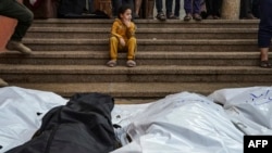 Mourners stand and sit near the shrouded bodies of loved ones killed during the Israeli bombardment of Nasser Hospital in Khan Younis in the southern Gaza Strip, Dec. 27, 2023.