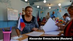 Избиратель перед членами избирательной комиссии на избирательном участке во время местных выборов в Донецке, контролируемая Россией Украина, 8 сентября 2023 года.