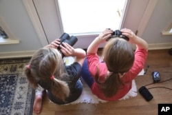This image provided by Macaulay Library/Cornell Lab of Ornithology shows two girls watching birds through a window with binoculars, bird lists and cameras in Elm Grove, Louisiana, during the Great Backyard Bird Count in February 2022. About 385,000 people from 192 countries took part in the 2022 count, and their results have been used by scientists to study bird populations worldwide. (Emily Tubbs/Macaulay Library/Cornell Lab of Ornithology via AP)