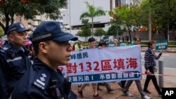 Polisi menyaksikan pengunjuk rasa berjalan di dalam garis penjagaan dengan mengenakan nomor tag saat unjuk rasa di Hong Kong, 26 Maret 2023. (Foto: AP)