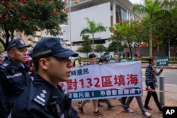 Police watch protesters walking within a cordon line wearing number tags during a rally in Hong Kong, March 26, 2023.