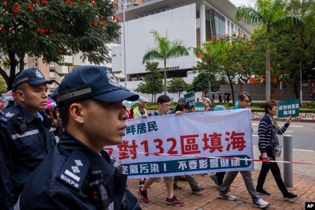 Police watch protesters walking within a cordon line wearing number tags during a rally in Hong Kong, March 26, 2023.