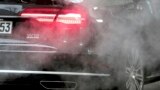 FILE - A luxury car is surrounded by exhaust gases as it is parked with a running engine in front of the Chancellery in Berlin, Germany, Nov. 20, 2019.