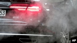 FILE - A luxury car is surrounded by exhaust gases as it is parked with a running engine in front of the Chancellery in Berlin, Germany, Nov. 20, 2019.