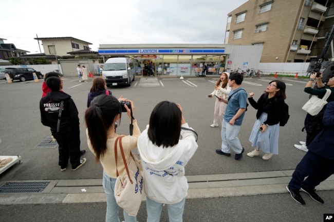 Tourists take pictures in front of the Lawson convenience store, a popular photo spot framing a picturesque view of Mt. Fuji in the background on cloudy evening of Tuesday, April 30, 2024, at Fujikawaguchiko town. (AP Photo/Eugene Hoshiko)