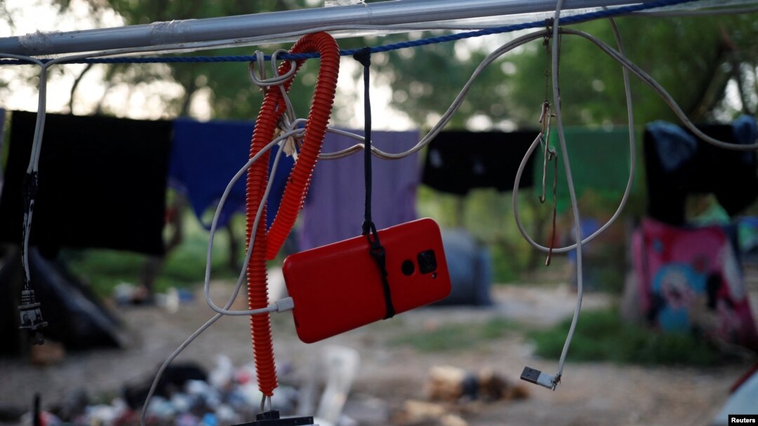 El teléfono celular de un solicitante de asilo cuelga mientras recarga la batería, a la espera de cruzar a EEUU con una cita a través de la aplicación de Aduanas y Protección Fronteriza, en un campamento improvisado en Matamoros, México, el 21 de junio de 2023.