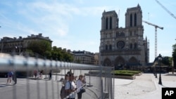 People watch Notre Dame cathedral from outside the security zone set up for the Olympic Games in Paris, July 18, 2024. 