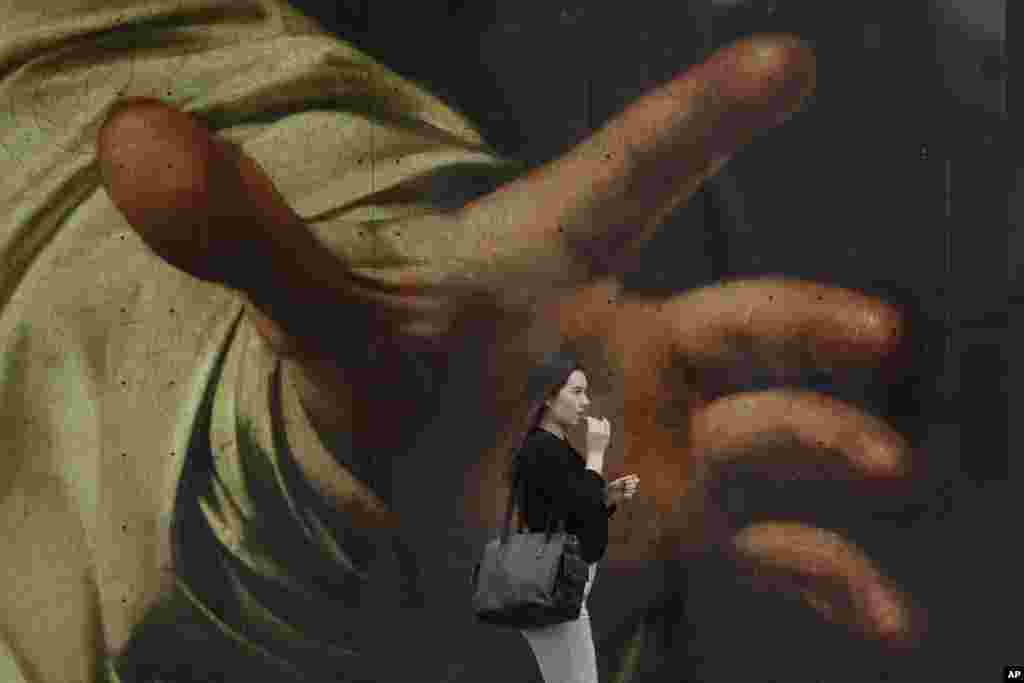 A woman walks past a poster featuring the painting of Caravaggio&#39;s &quot;The Supper at Emmaus&quot; outside the National Gallery, in London. (AP Photo/Kin Cheung)