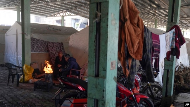 FILE - Syrian refugees warm themselves by a fire in front of tents set up in a public market space as shelter in Islahiye District of Gaziantep, southern Turkey, Feb. 11, 2023.