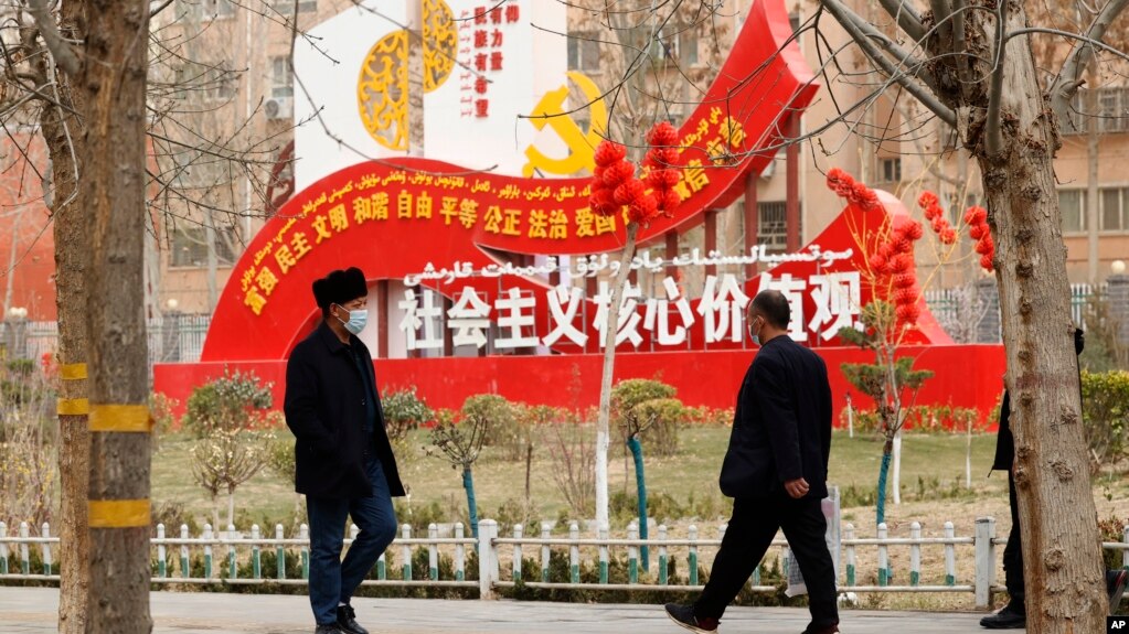 资料照:新疆和田居民走过街头竖立的社会主义核心价值观的宣传牌。(2021年3月22日)