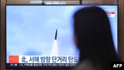 A woman walks past a television showing a news broadcast with file footage of a North Korean missile test, at a railway station in Seoul on March 9, 2023.
